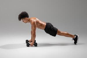 A fit young man engages in a rigorous workout by executing dumbbell push-ups in a well-lit studio gym. He maintains proper form while focusing on strength training and building muscle endurance photo