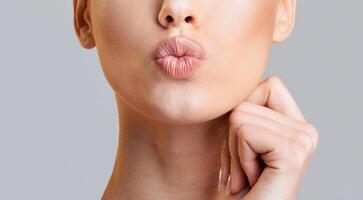 Cropped of woman face, showcasing her lips as they pout in a slightly seductive expression. She has a hand resting on her chin, adding a touch of sensuality to the overall pose, cropped photo