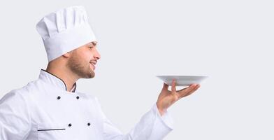 Professional Chef Holding Empty Plate Serving Invisible Dish Standing On White Background. Side View, Studio Shot, Panorama photo
