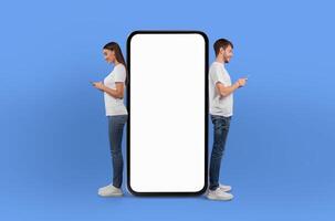 A man and woman are standing next to a large screen phone, appearing to be engaged in a conversation or viewing content on the device. Both individuals seem focused on the screen in front of them. photo