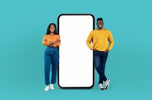 Happy black couple stand, a smile on each of their faces, next to a large smartphone that features a blank screen, providing a versatile backdrop for creative projects. photo