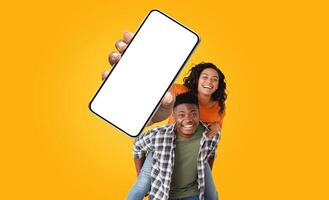 African American young couple is smiling and looking at the camera, woman holds a large smartphone with a blank screen in front of them photo