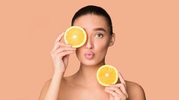 Playful woman holds a slice of orange over her eyes, showcasing a moment of relaxation and self-care. With closed eyes, she enjoys the citrus scent and potential benefits of the fruit photo