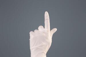 Hand wearing latex gloves gesturing upward on grey background, pushing button on virtual touchscreen photo