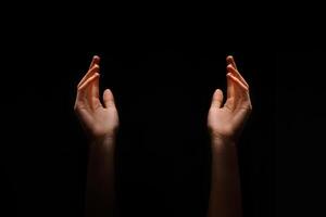 This image shows two hands reaching upward in the dark. The hands are positioned symmetrically, with their palms facing upwards. photo