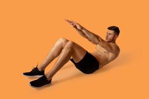 A man is seen doing an exercise against a vibrant orange background. He is focused and engaged in his workout routine, displaying strength and determination. photo