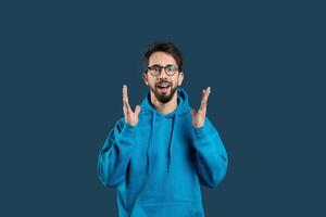 A man wearing a blue hoodie is seen gesturing with his hand in this photograph. The gesture appears to be deliberate and expressive, drawing attention to his actions. photo