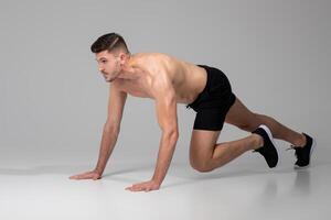 A man is performing push ups on a gray background. He is using his hands and feet to lift and lower his body repeatedly in a strength-building exercise. photo