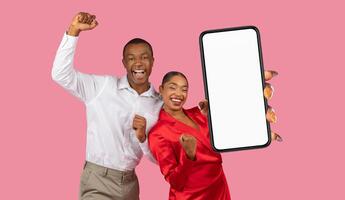 A young black couple, smiling and have their fists raised in the air as if they are celebrating. The woman is holding a large smartphone in front of them, and the screen is blank. photo