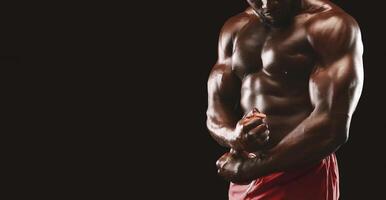 A close-up shot of a muscular man flexing his biceps, showcasing his defined physique. He is wearing red shorts and standing against a black background. photo