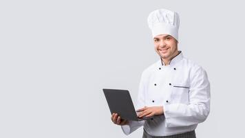 Chef Man Using Laptop Browsing New Recipes Standing On White Studio Background. Culinary Website. Panorama photo