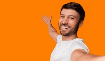 Check This Out. Positive Man Taking Selfie And Showing At Free Space Over Yellow Studio Background. photo