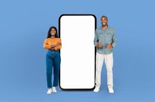 African American man and woman are standing side by side, looking at a blank phone screen. They appear to be discussing something as they both focus on the device in their hands. photo