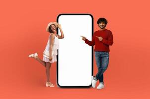 A man and woman are standing side by side next to a landline phone with a blank screen. The man appears to be talking while the woman is looking at the phone. The setting seems to be indoors. photo