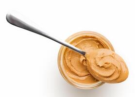 Peanut butter in glass jar and spoon isolated on white background, top view, copy space. American dessert concept photo