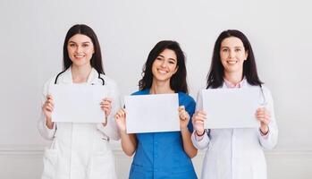 Medical Information. Doctors And Interns Holding Empty Papers, Standing In Hospital Over Grey Wall photo