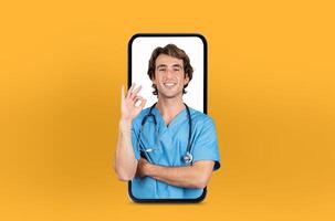 Featuring modern telehealth services, this image shows a young man doctor on a smartphone screen, isolated on yellow studio background photo