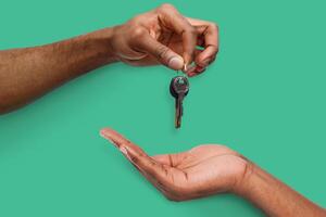 Black male hand holding new key and handing it over to another person on turquoise background photo