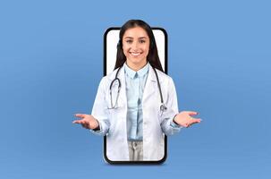 A woman wearing a white coat is standing in front of a telephone. She appears to be interacting with the phone, possibly making a call or sending a message. photo