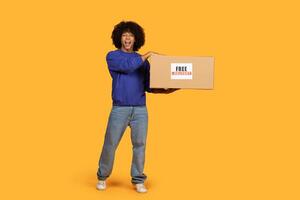 A man is standing and holding a box, which has a free delivery sign on it. He seems to be ready to deliver the package to a customer. photo