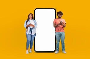 Multiethnic lovers seen standing next to a large telephone, looking up at it in curiosity. The man is holding a smartphone, while the woman points at the oversized phone. photo