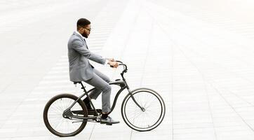 An African American professional is cycling through the city. The setting is urban and busy, highlighting the blend of business efficiency and active commuting. photo