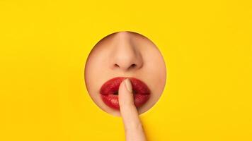 A close-up view of a woman gently touching her red lips on a bright yellow background. The contrast between the colorful backdrop and the soft texture of the lips creates a simple yet impactful image. photo