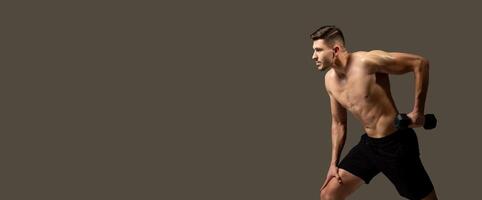 A man is actively engaged in a dumbbell exercise, lifting weights with focused determination against a plain gray background, panorama with copy space photo