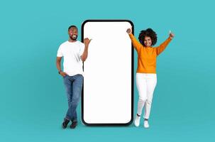 Black man and woman are standing side by side, looking at a blank screen on a phone. Both are focused on the device, potentially discussing something or waiting for information to appear. photo