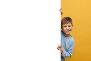 A young boy is pictured holding a white sign in this photograph. He appears to be standing outdoors, with a serious expression on his face as he grasps the sign firmly. The sign is blank photo