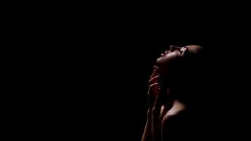 A woman with her head tilted back, looking towards the top of the frame, is silhouetted against a dark background. She has her fingers gently on her neck, copy space photo