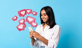 Indian millennial woman scrolling via smartphone, chatting online on blue studio background. Happy lady browsing, using modern dating application photo