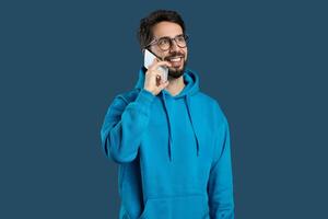 A man wearing a blue hoodie is engaged in a conversation on his cell phone. His attention is focused on the call as he stands in a public area. photo