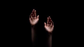 Two hands reaching up towards the dark, unknown, or possibly a source of light, suggesting a sense of hope or desperation, appear to be reaching out for something. photo