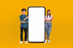 A man and a woman are standing side by side next to a large phone. The man is holding a notepad and pen while the woman looks at the phone screen. They appear to be discussing something important. photo