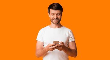 Mobile App. Happy Man Using Cellphone Standing Over Yellow Studio Background. Panorama With Copy Space photo