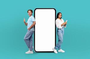 Multiethnic couple stand, a smile on each of their faces, next to a large smartphone that features a blank screen, providing a versatile backdrop for creative projects. photo