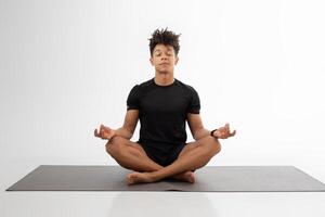 A man sits cross-legged on a yoga mat, eyes closed, in a state of deep concentration and tranquility. The spacious indoor setting highlights the calming atmosphere, encouraging mindfulness photo