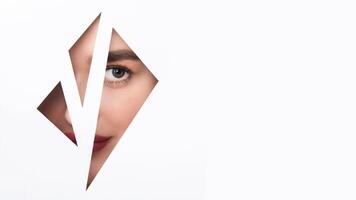A woman face emerges from holes in a stark white wall, her eyes wide in surprise. The hole is just big enough for her to peek through, creating a sense of curiosity and mystery. photo