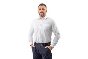 A man dressed in a crisp white shirt and dark trousers stands confidently with hands in pockets, looking directly ahead. He is captured against a plain white backdrop photo