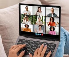 Nine individuals participate in an online conference. Each person is visible in their individual boxes, showing various gestures and expressions, sitting on a couch in a casual setting. photo