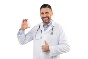 A man doctor with a stethoscope around neck smiles while holding a white medication bottle in one hand and giving a thumbs up with the other, conveying approval and confidence in a clinical setting. photo