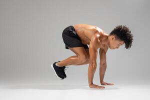 A fit young man engages in an athletic movement, focusing on strength and agility. He demonstrates a powerful stance in preparation for a dynamic workout, showcasing his dedication to fitness photo