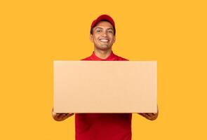A man wearing a red shirt is seen grasping a cardboard box in his hands. The man appears to be standing upright, firmly holding onto the box with a focused expression on his face. photo