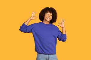 A cheerful man is smiling broadly while making the okay gesture with both hands. The vibrant yellow background enhances the lively atmosphere, emphasizing the guy's joyful expression photo