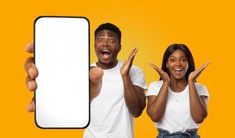 African American young man and woman are holding a smartphone with a blank screen. They are both smiling and looking excited. photo