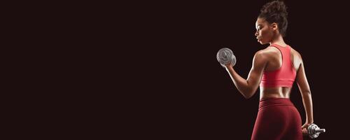 Black fitness lady doing workout with dumbbells, back view, black studio background, panorama with copy space photo