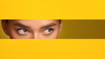 A close-up of a woman eyes filling the frame, set against a vibrant yellow paper wall background. The woman features are visible, showcasing her eyes, nose, copy space photo