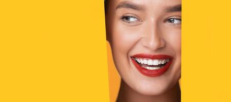A woman face is partially visible through a round hole in a bright yellow background. She appears to be looking directly at copy space, with a neutral expression, panorama photo
