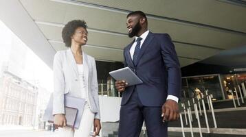Two smiling african american colleagues discussing new project while going out of office building, copy space photo